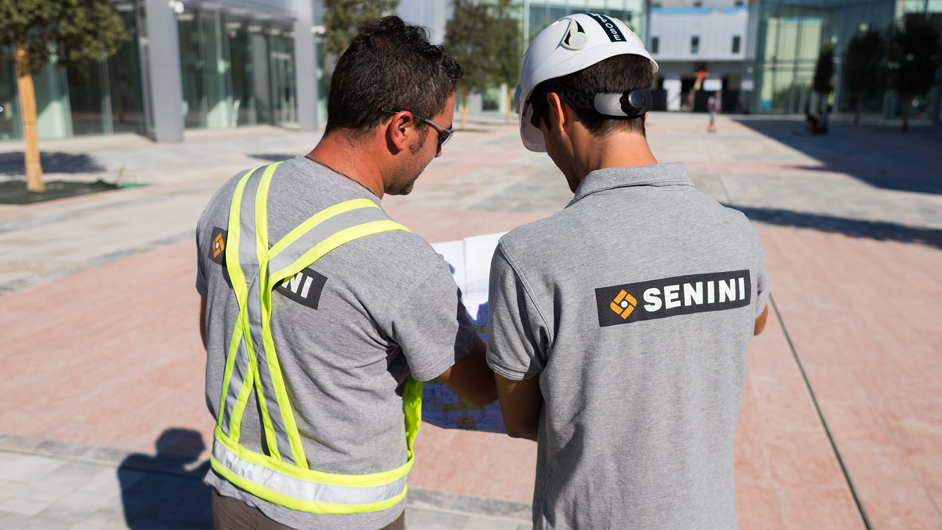 a two men wearing matching shirts of Senini's brand and helmets looking at a map